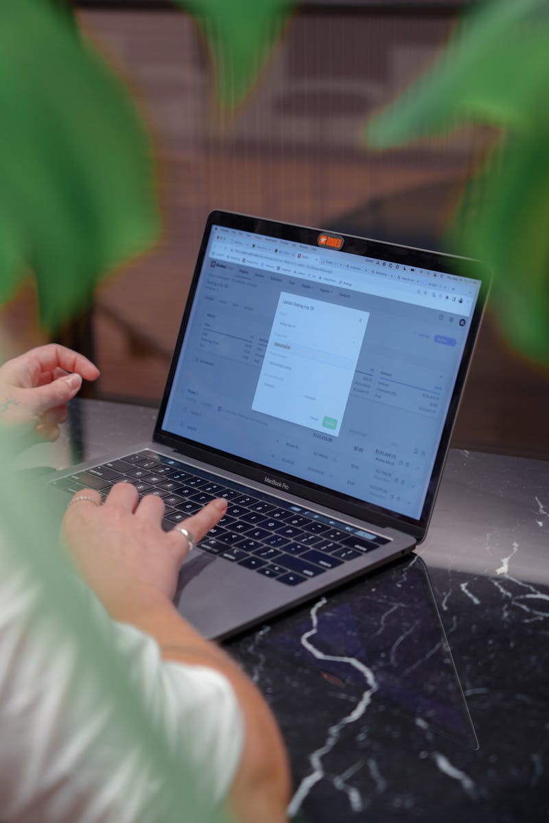 Close-up of a man typing on a laptop, surrounded by green plants, in a cozy indoor setting.